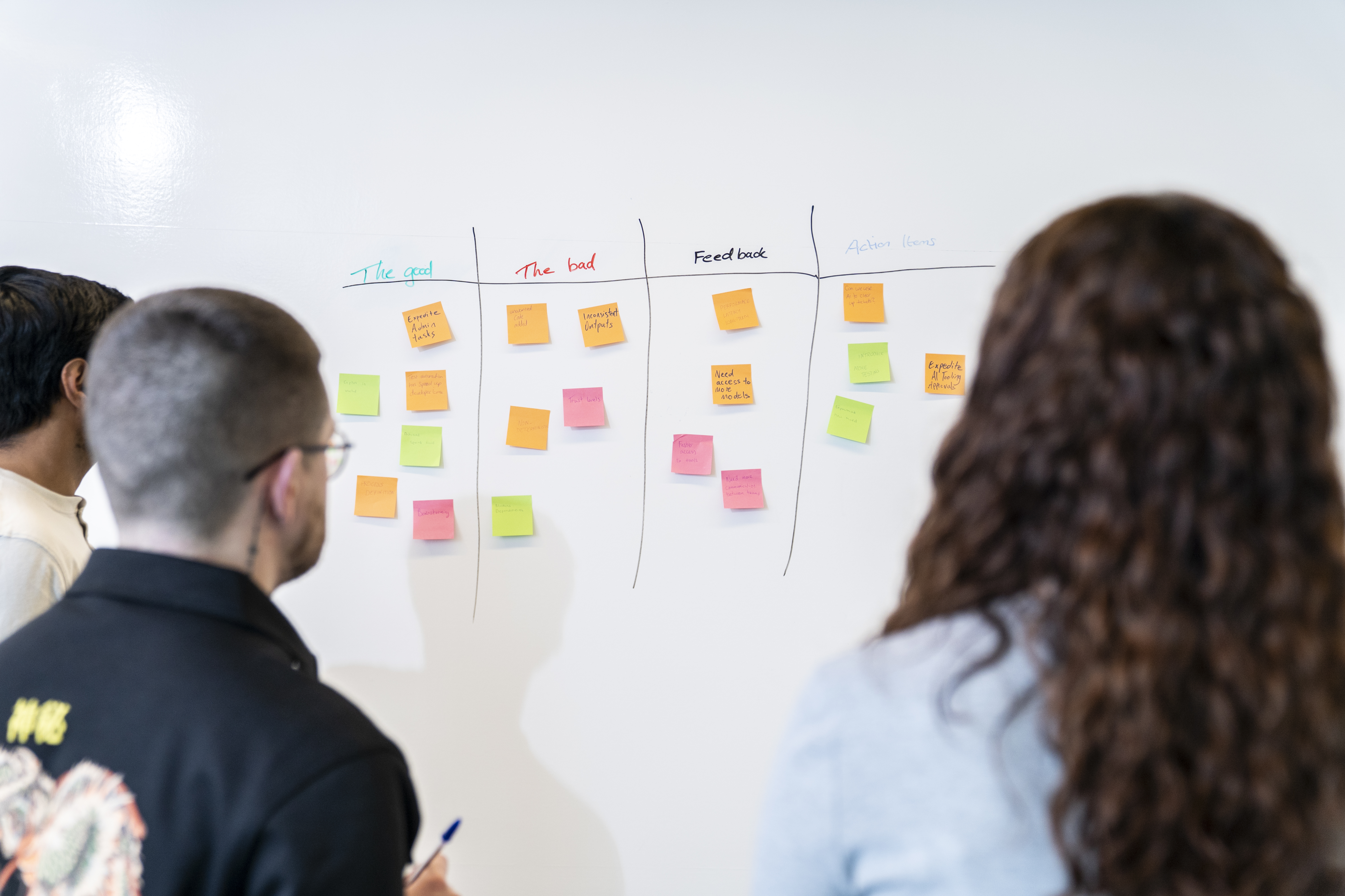 Three Liberty IT employees looking at a whiteboard with post-it notes 
