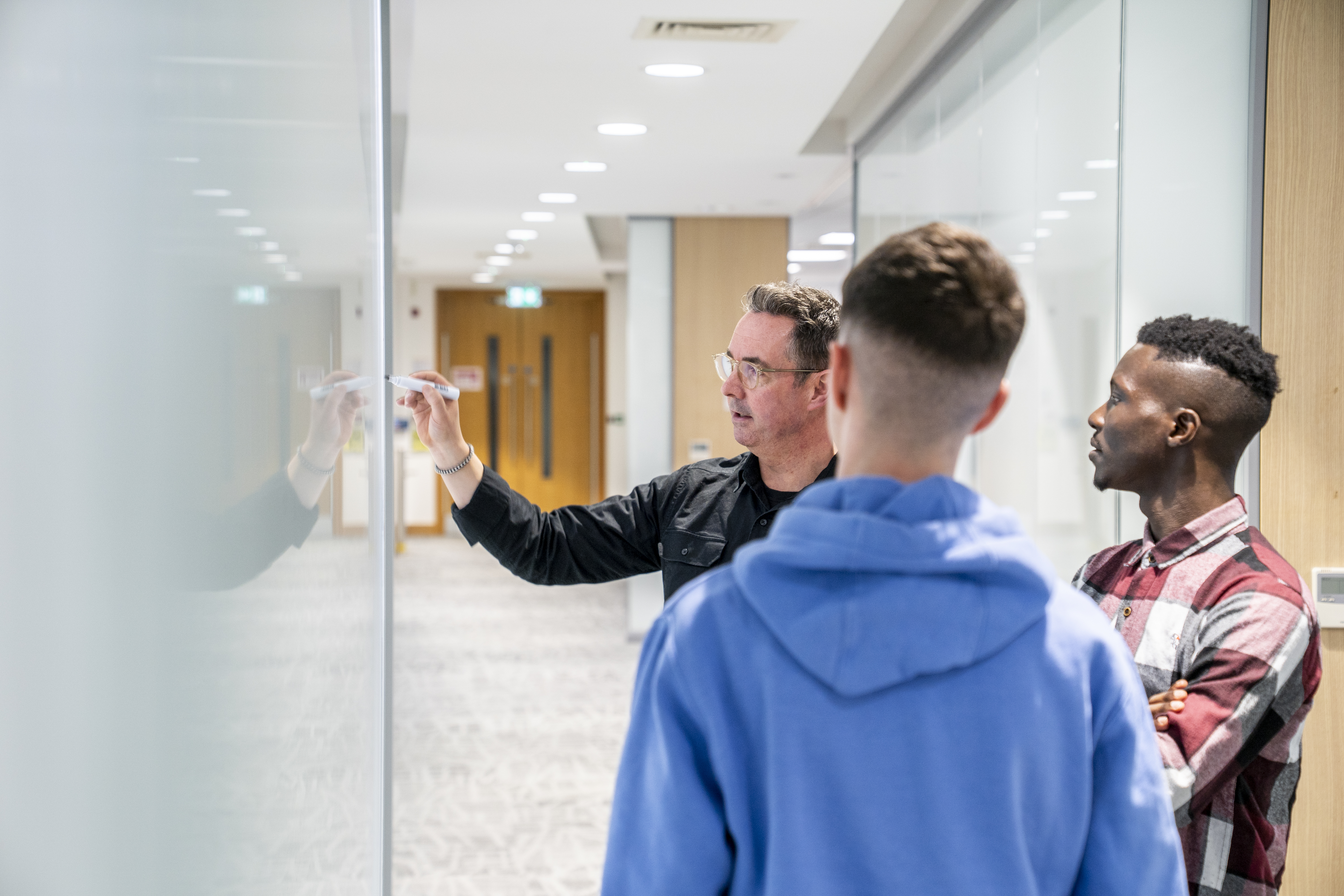 Employees discussing ideas at a whiteboard in a Liberty IT office hallway.