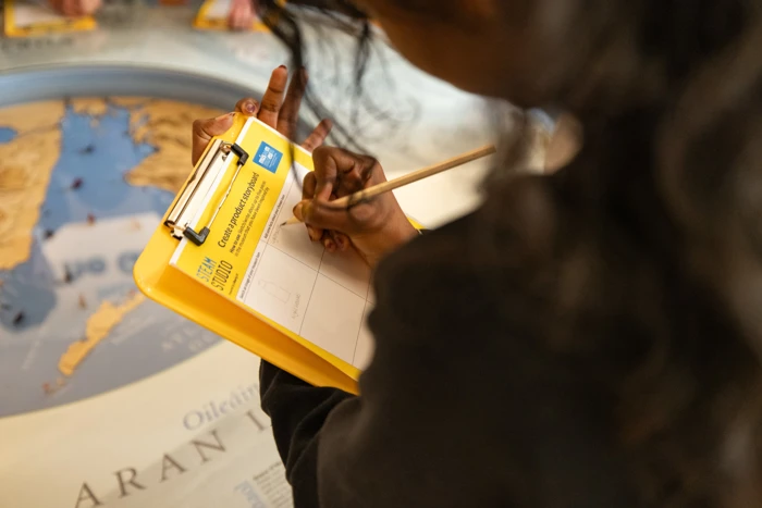 A student writing on STEAM Studio activity paper during a session