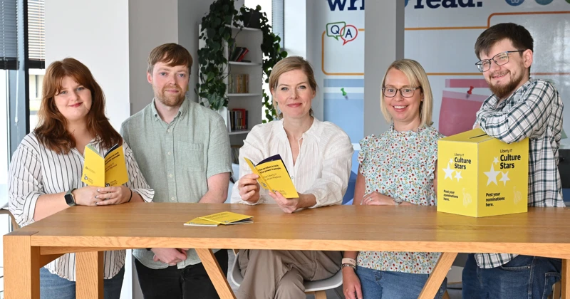 Five employees smiling in an office with Liberty IT culture books
