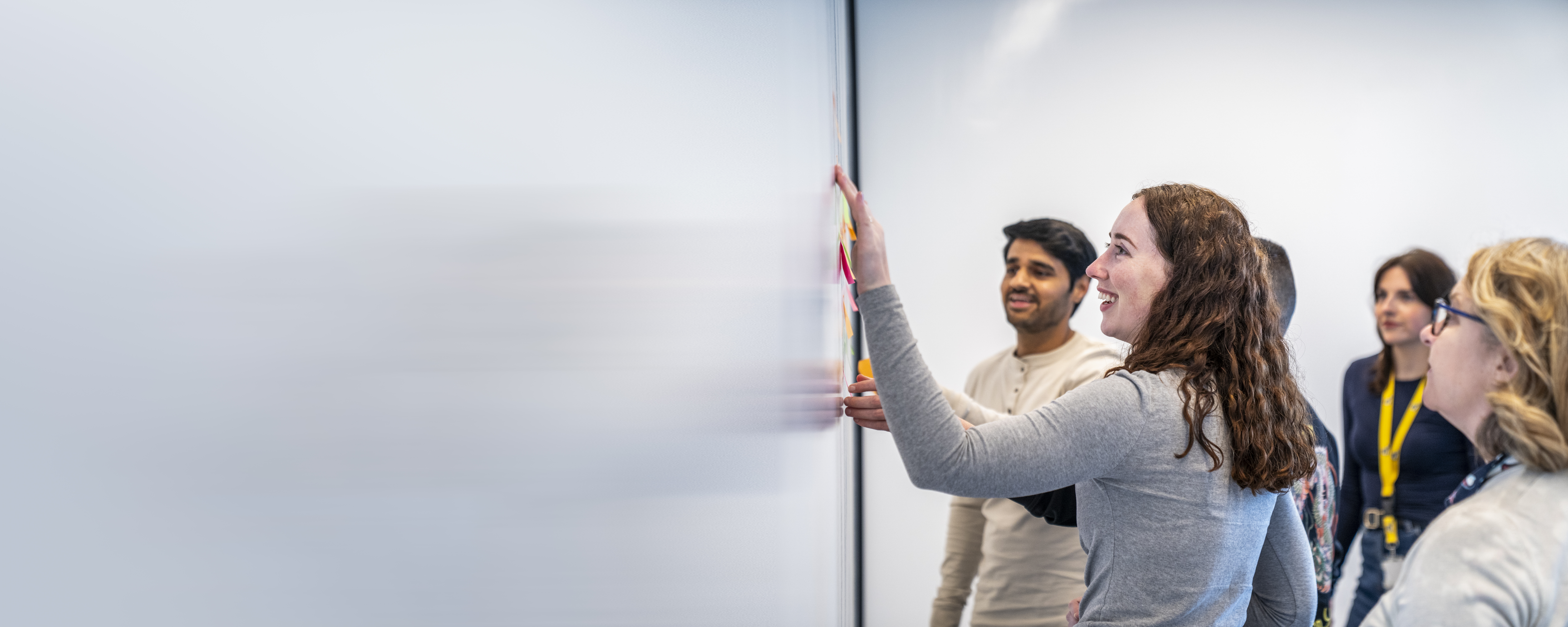 Employees whiteboarding with one employee smiling and placing a post-it note on the wall
