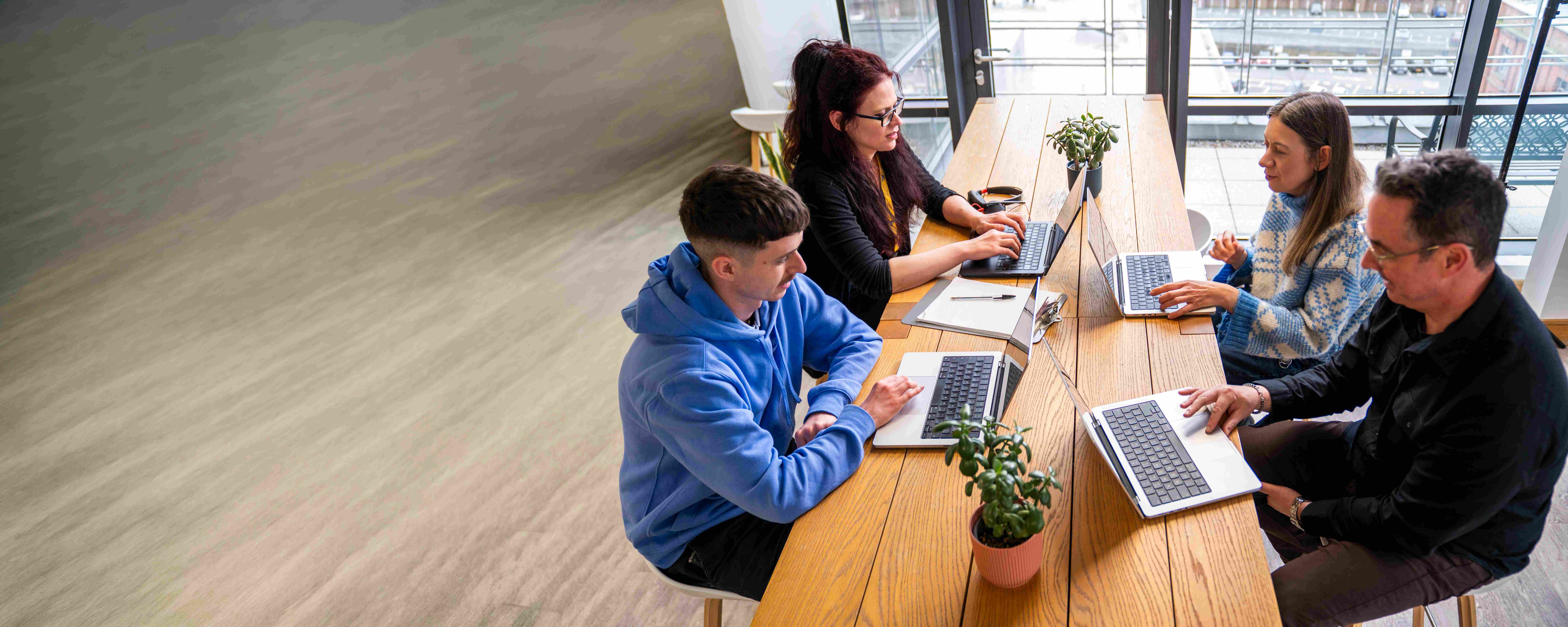 Four employees gathered around a table on their laptops