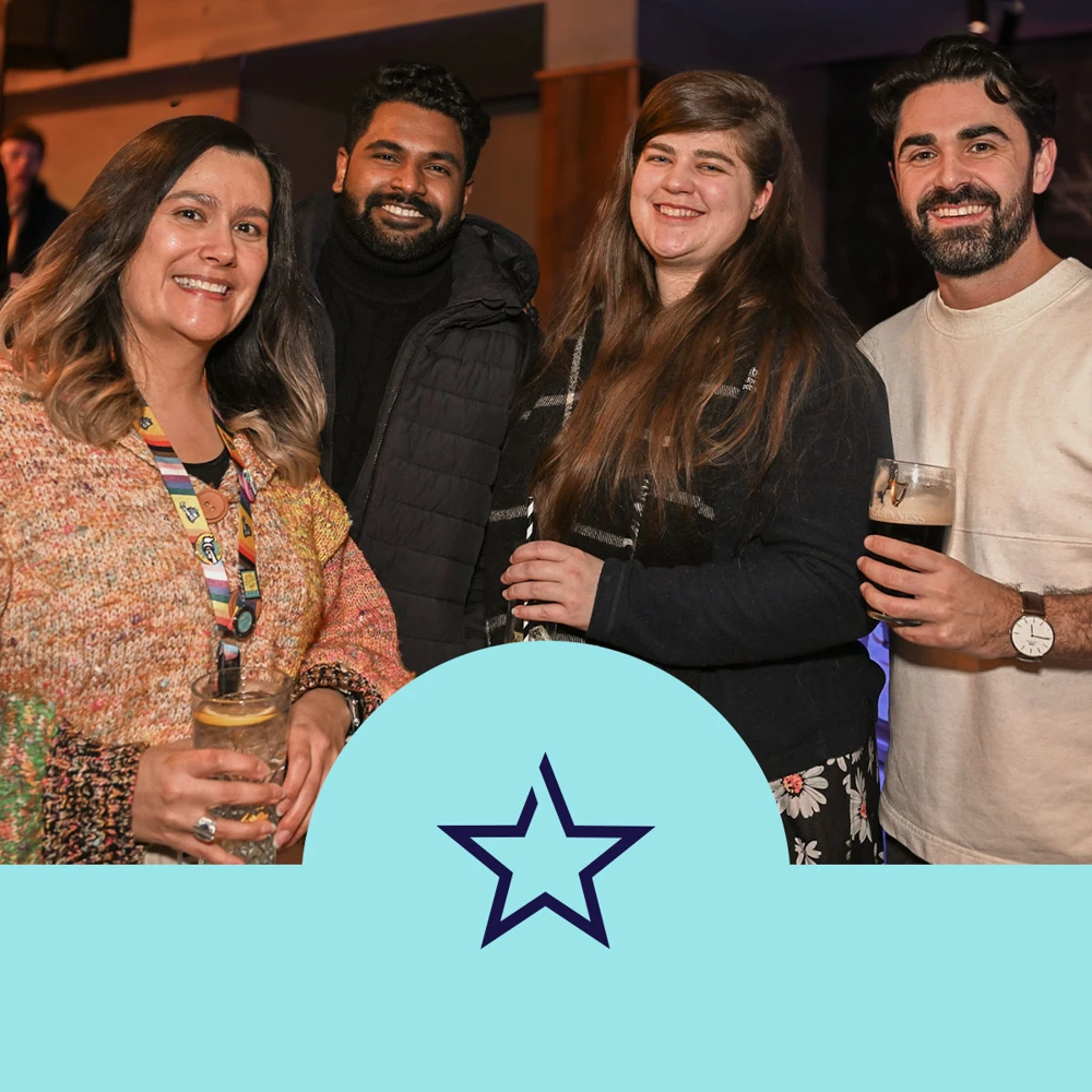 Group of four people posing for a photo. A logo with a star is displayed at the bottom center.