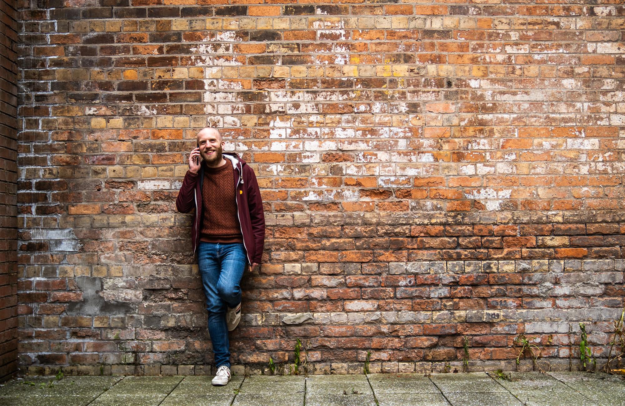 Photo of man standing in front of brick wall, on his phone